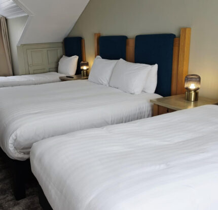 Spacious hotel room with three cosy double beds, soft white linens, elegant bedside lamps, and a tranquil ambience.
