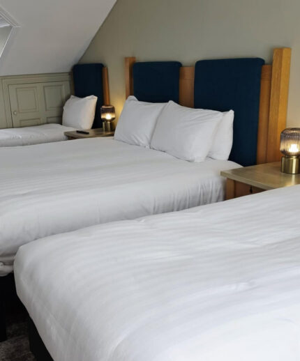 Spacious hotel room with three cosy double beds, soft white linens, elegant bedside lamps, and a tranquil ambience.